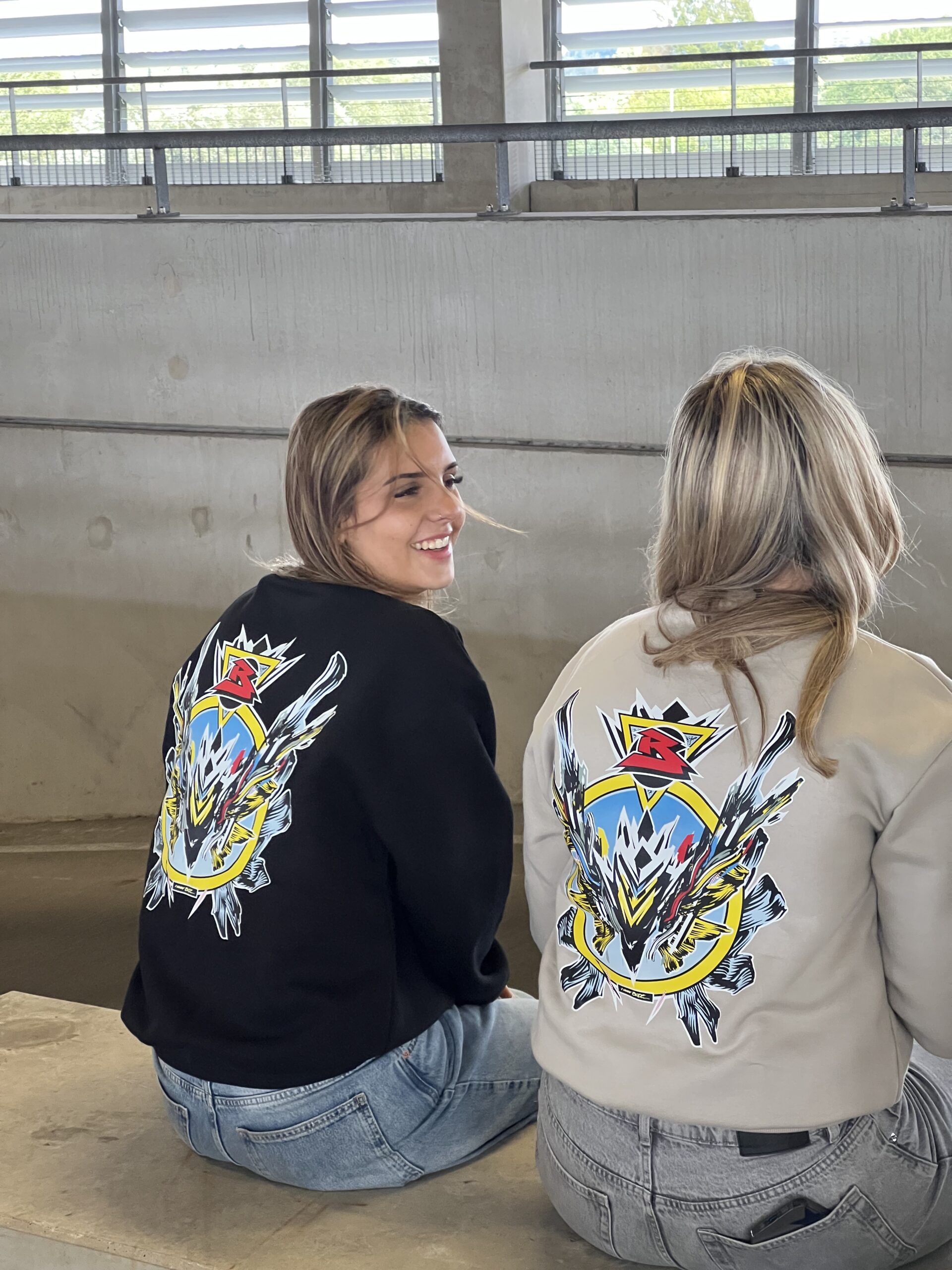 Duo foto met BRIDGE sweaters in zwart en beige, exclusief design van kunstenaar Luuk Bode, unisex streetwear in maat M, L en XL