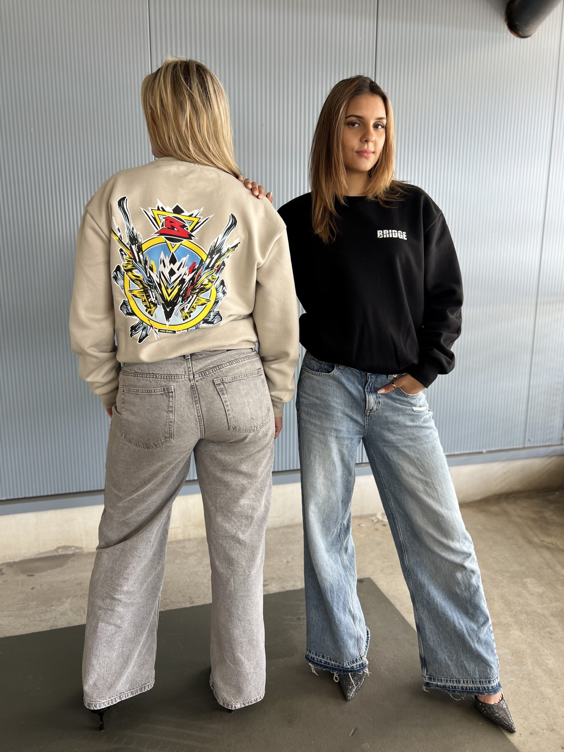 Duo foto met BRIDGE sweaters in zwart en beige, exclusief design van kunstenaar Luuk Bode, unisex streetwear in maat M, L en XL